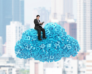 Big data and cloud computing concept. Sitting businessman using digital tablet on cloud of blue letters and numbers, on city buildings cityscape background. 