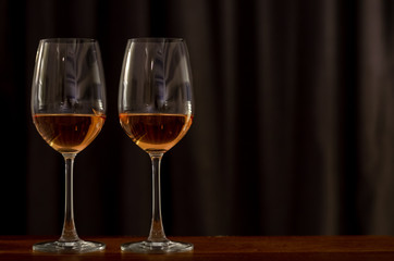 Two glasses of Rose wine on wooden table to celebrate for a couple with dark background of curtain in the house.