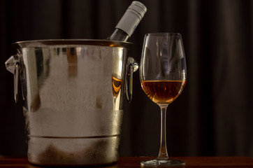 A glasses of Rose wine on wooden table with a bottle in wine chiller bucket to celebrate with dark background in the house.
