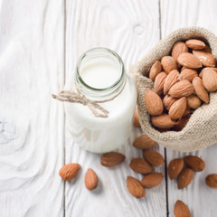 Milk or yogurt in glass bottle on white wooden table with almonds in hemp sack aside