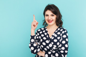 Smiling woman on a blue background pointing something by her finger