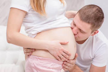 Young husband kisses to the belly of his pregnant wife on the bed