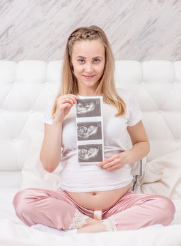 Pregnant woman holding ultrasound scan on the bed at home
