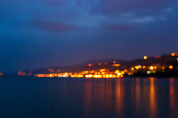 Naklejka na ściany i meble Blurred cityscape with light bokeh and sea