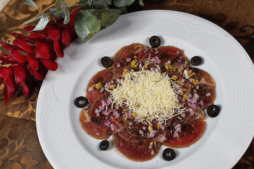 Carpaccio de res with black olive, purple onion and grated cheese