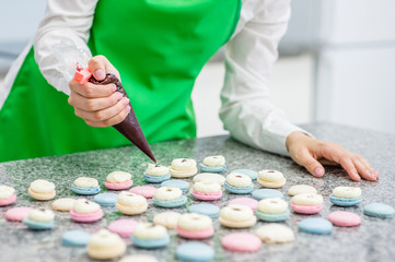Closeup chef with confectionery bag squeezing cream filling to macarons shells