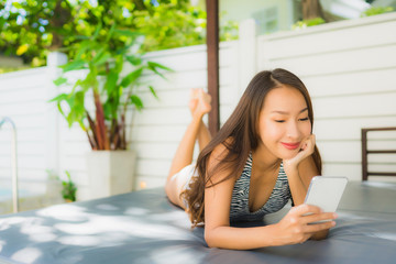 Portrait beautiful young asian woman smile happy relax with mobile phone around swimming pool in hotel resort for leisure