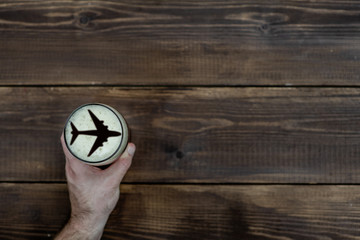 man's hand holds a mug of beer with silhouettes of a airplane on dark wooden background