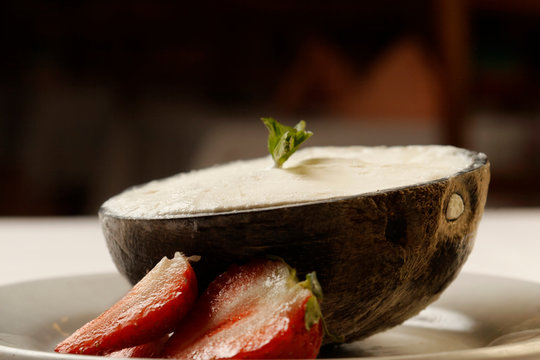 Dessert of coconut ice cream inside coconut shell accompanied by strawberries.