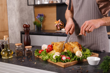 Hands of chief man cuting baked chicken with vegetables