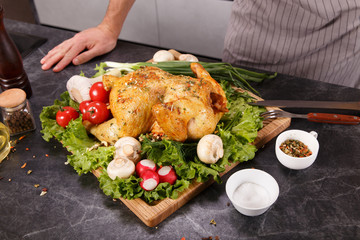 Hands of chief man cuting baked chicken with vegetables