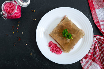 Meat jelly with spicy horseradish on a white plate on a black background. Slavonic traditional cold dish. Top view, flat lay