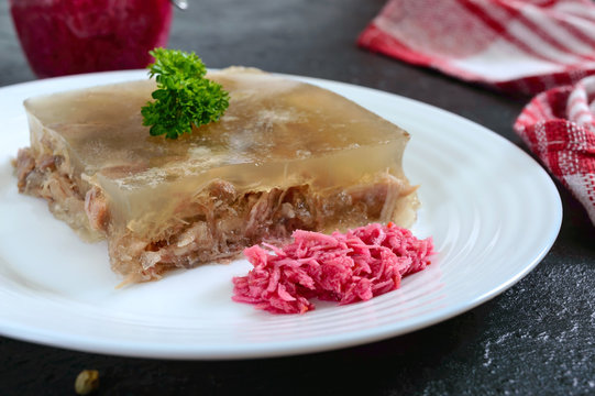 Meat jelly with spicy horseradish on a white plate on a black background. Slavonic traditional cold dish. Close-up