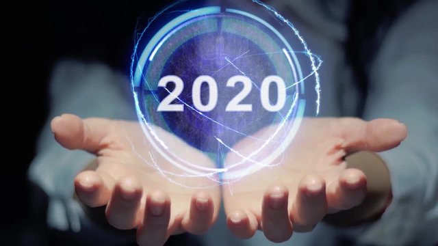 Female hands show a round conceptual hologram with text 2020. Unrecognizable woman in ashen white on a black background with future holographic technology
