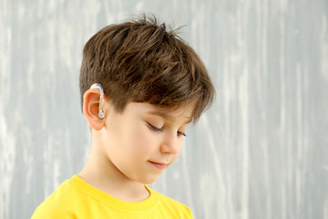 Little boy with hearing aid on grey background