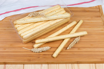 Breadsticks with sesame seeds and wheat ears on wooden surface