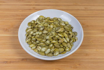 Peeled pumpkin seeds on saucer on a wooden surface