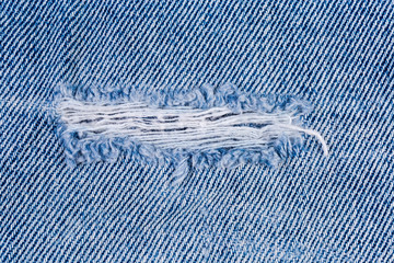 Hole on denim jeans with frayed threads close-up