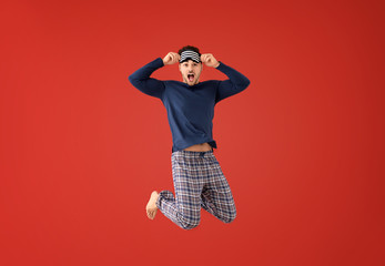 Jumping young man in pajamas with sleep mask on color background