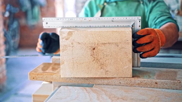 Man in protective uniform with mask measures the stone slabs in factory. Worker with the ruler is measuring cutted stone slabs in the industrial manufacture.