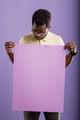 Picture of young african american man holding blank board on violet background