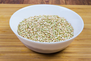 Bowl of uncooked not steamed buckwheat groats on wooden surface