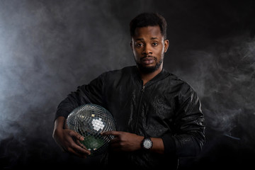 Young cool black man with disco ball over black background