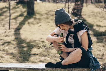Poor homeless woman with bottle sitting on bench outdoors
