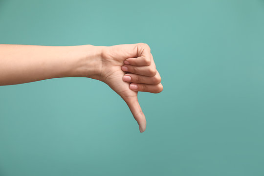 Female hand showing thumb-down gesture on color background