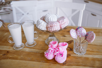 milk, marshmallows, sweets, flowers, pink children's shoes on the kitchen table, decor for pregnancy photo shoots