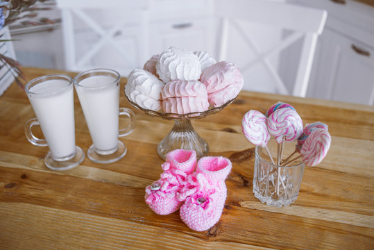 milk, marshmallows, sweets, pink baby shoes on the kitchen table, decor for pregnancy photo shoot