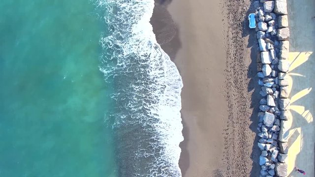 Birds eye view of waves crashing on beautiful sandy beach with a line of rocks and people walking also people cycling. 
shot on a stretch of coast line called the "milla de oro" "golden mile"