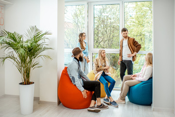 Group of diverse people having a conversation during the coffee break sitting on the colorful poufs...
