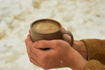Male hand holding cup of coffee with snowy background 