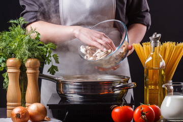 young woman in a gray apron roasts mushrooms in a frying pan