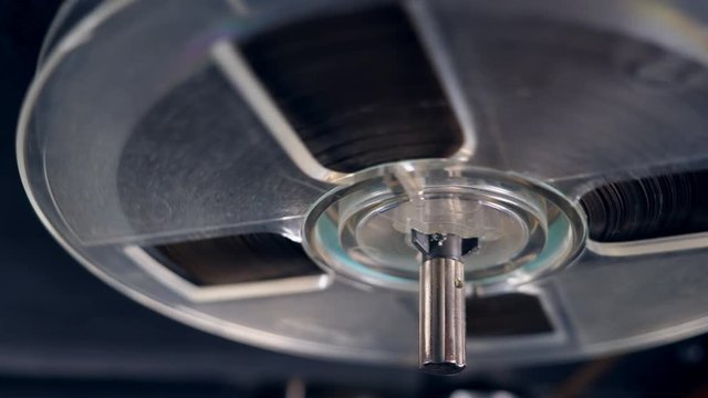 Round spool with tape slowly spins on a magnetic recorder.