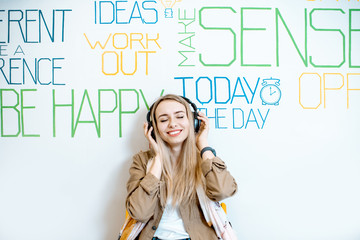 Portrait of a young smiling woman with headphones on the wall background with various inscriptions on the topic of mental health