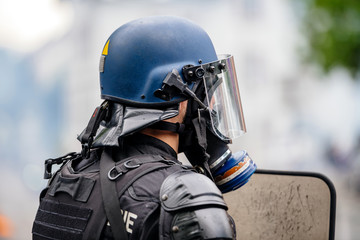 Rear view of police officer wearing gas mask against tear gas at protest with Yellow jackets Gilets...