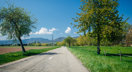 Car driving on the empty road towar Vosges mountains in France clear blue sky and green grass