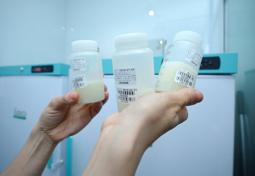 At The Human Milk Bank Laboratory. Lab Assistant Hands Holding  Breast Milk Storage Containers With Human Milk Inside, Freezers On A Background