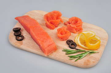 Fresh salmon decorative roses fillets, with lemon, olives on the board. Isolated on a gray background