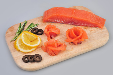 Fresh salmon decorative roses fillets, with lemon, olives on the board. Isolated on a gray background
