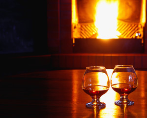 Fototapeta na wymiar Two glasses of cognac on the old brick fireplace with bright fire