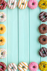 Donuts of different flavors for breakfast frame on mint green wooden background top view space for text