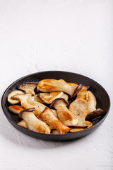 Fried eryngii mushrooms in cast-iron pan on white table. Grilled slices of king oyster mushrooms. Copy space.