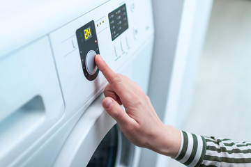 Housewife using display and button for turning on and choosing cycle program on washing machine for laundry at home.