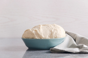 Risen raw dough for pizza in the blue bowl on the kitchen table