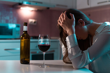 Fototapeta Unhappy, lonely, young woman with red wine is drinking alone at home in evening. Life difficulties and problems. Female alcoholism and alcohol addiction obraz