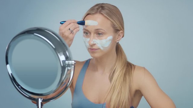 young blond model cover her face with blue clay cleansing mask