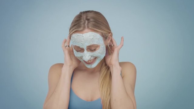 blond woman with face covered with blue facial mask have fun smiling and making faces